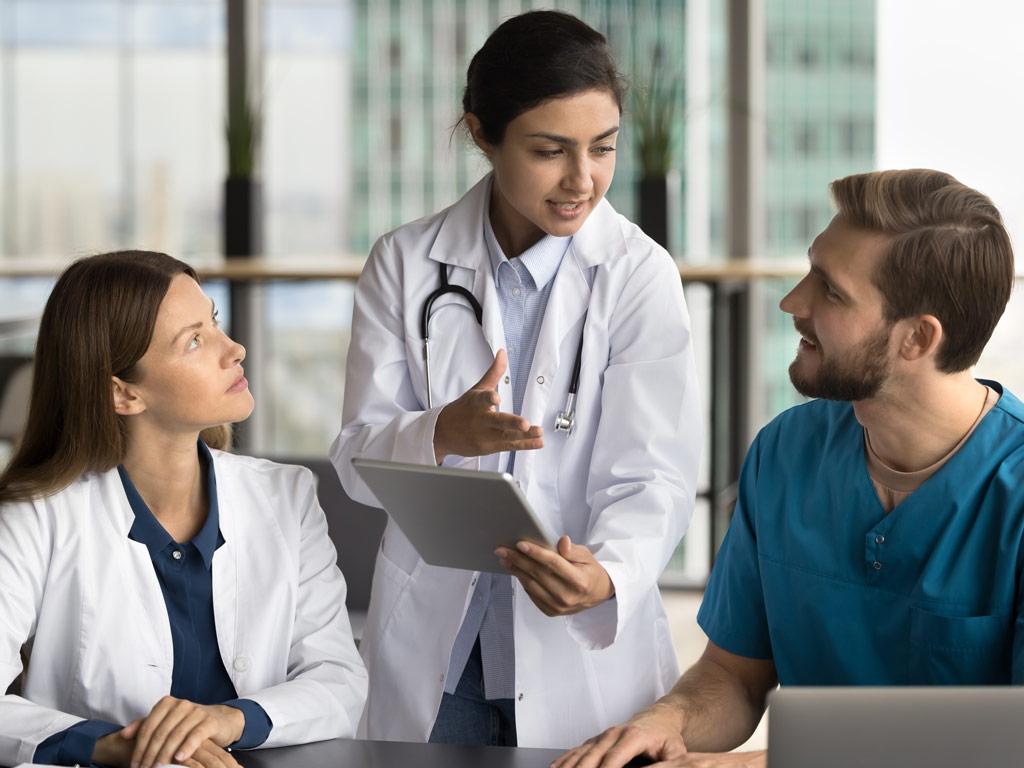 standing doctor speaking to two seated doctors